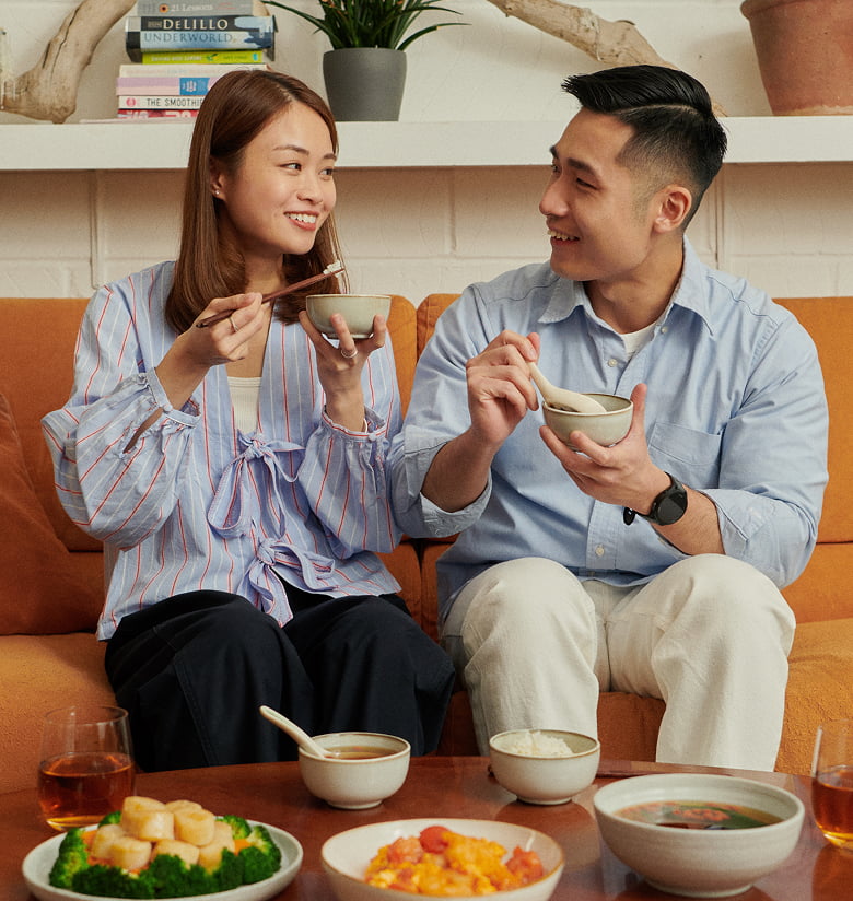 年輕情侶在橙色沙發上開心用餐的客廳照片